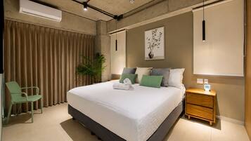 A modern hotel room with a large bed, a desk, a chair, and a potted plant.