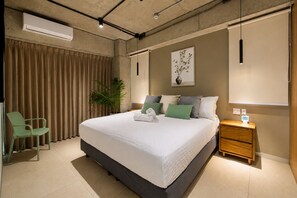 Habitació d'hotel moderna amb un llit gran, un escriptori, una cadira i una planta en test.