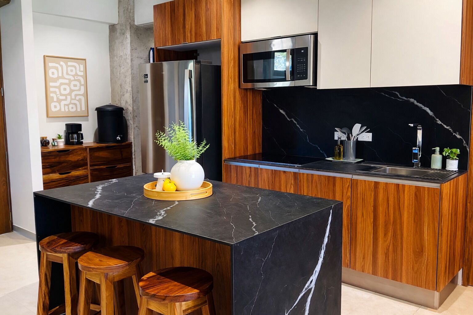 Una cocina moderna con una isla central, armarios de madera, microondas integrado y un salpicadero de mármol negro.