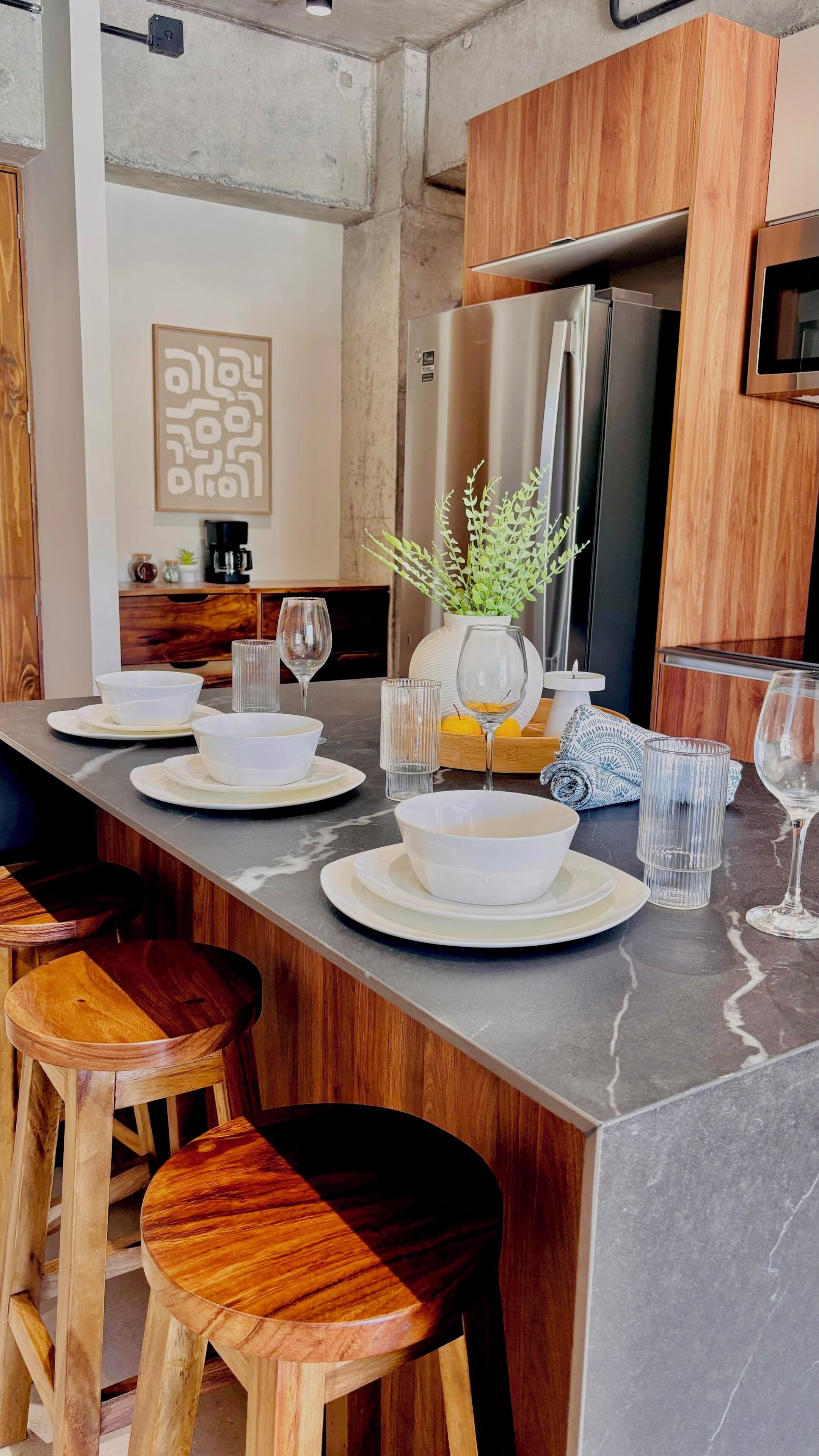 Una cocina moderna con encimera de mármol, taburetes de madera, refrigerador de acero inoxidable y una planta en maceta.