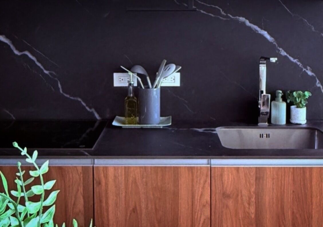 Una cocina con salpicadero de mármol, pileta de acero inoxidable y mueble de madera.