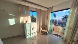 Une pièce spacieuse dotée d’une grande porte-fenêtre coulissante, d’une commode blanche et d’un fauteuil confortable.