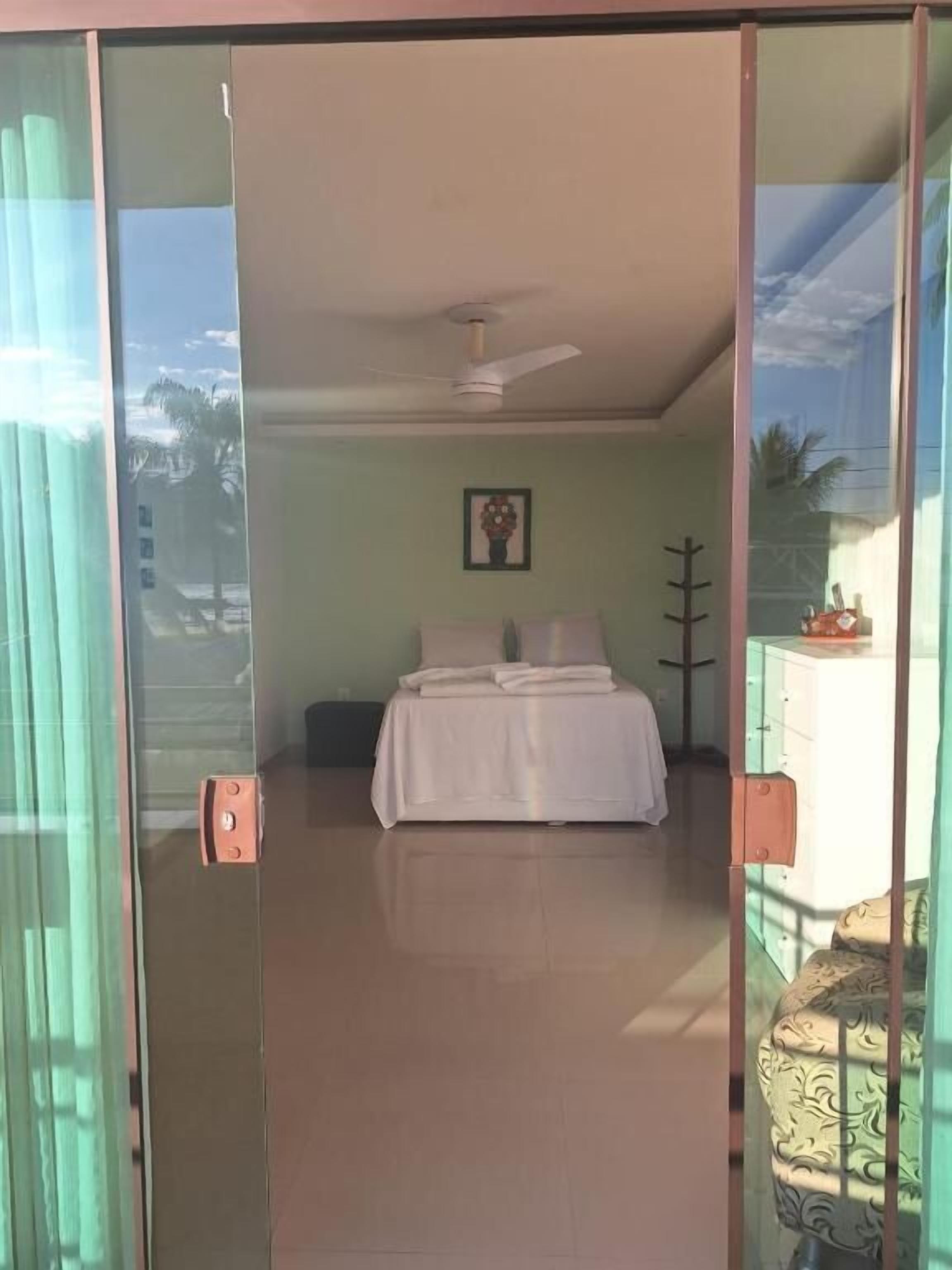 A bedroom with a bed, a ceiling fan, a framed picture on the wall, and a glass door leading outside.