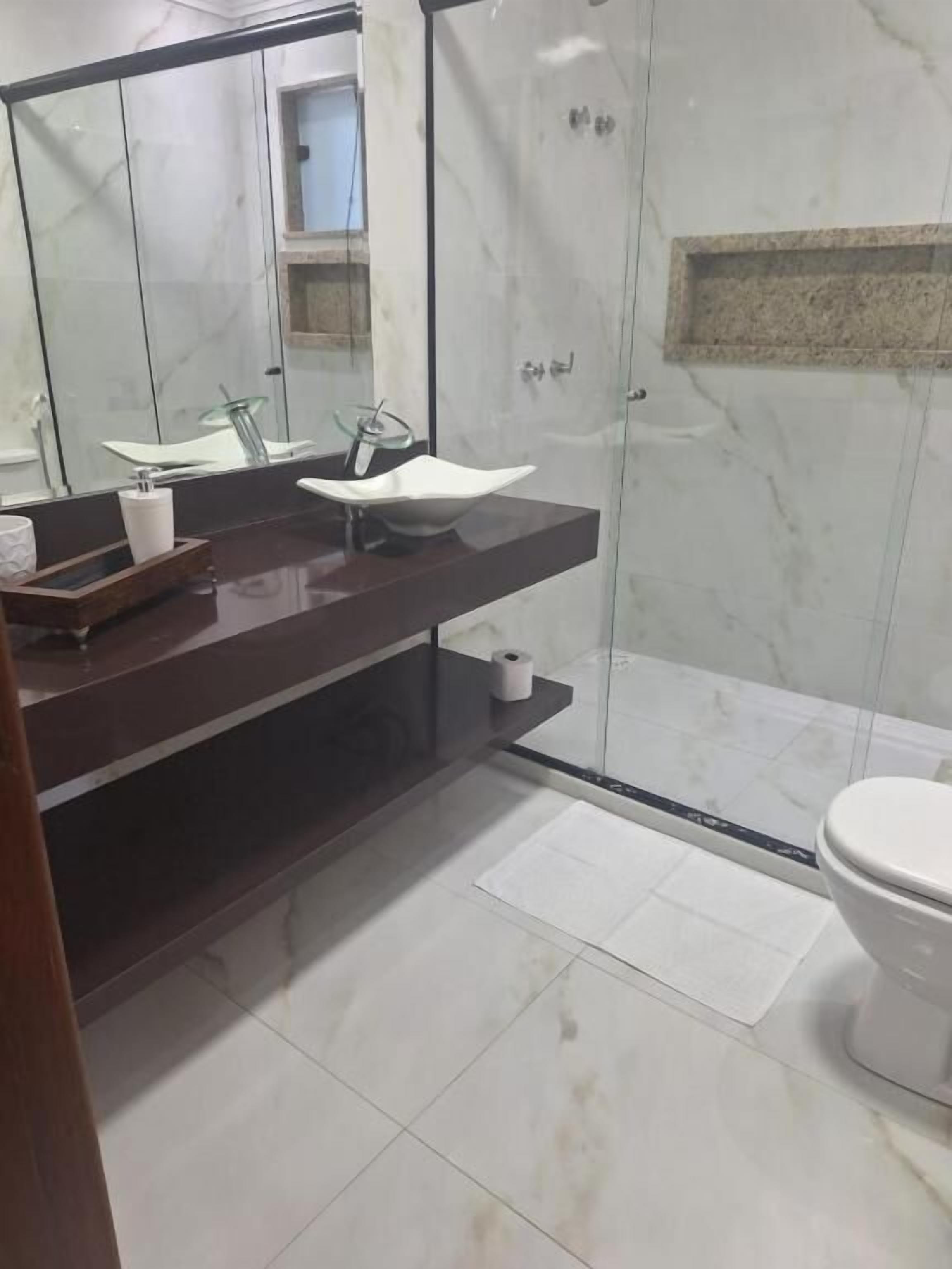 Casa de banho moderna com cabine de chuveiro em vidro, lavatório branco e sanita.