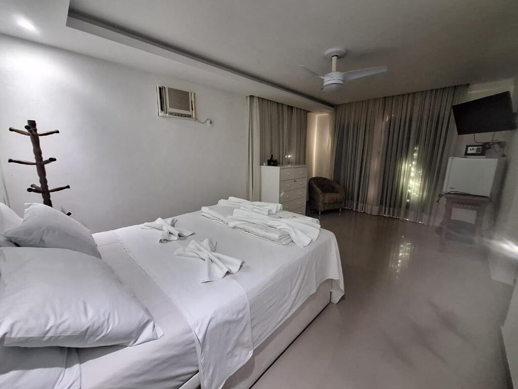 Una habitación de hotel con cama, una silla, escritorio, televisor y ventilador de techo.
