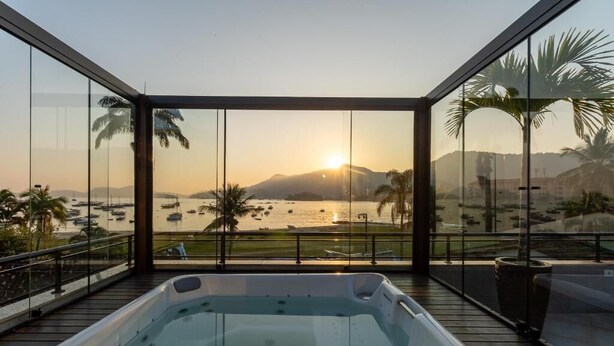 Un jacuzzi sur un balcon offrant une vue sur le coucher de soleil, avec un plan d’eau et des palmiers en toile de fond.