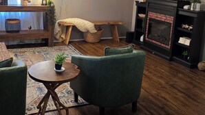 A living room with a fireplace, a television, and a green armchair. - Cozy Country Cottage in enchanting Statesboro with AC (Statesboro)
