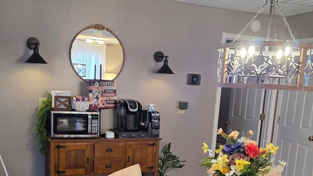 A dining area with a wooden table, chairs, a chandelier, a microwave, a coffee maker, and a mirror on the wall. - Cozy Country Cottage in enchanting Statesboro with AC (Statesboro)