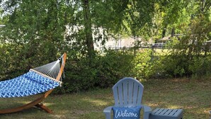 A backyard with a hammock, two Adirondack chairs, a fire pit, and a stone wall. - Cozy Country Cottage in enchanting Statesboro with AC (Statesboro)