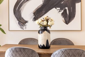 Een eettafel met een bloemenvaas, een lijst met abstract schilderij en grijs gestoffeerde stoelen.