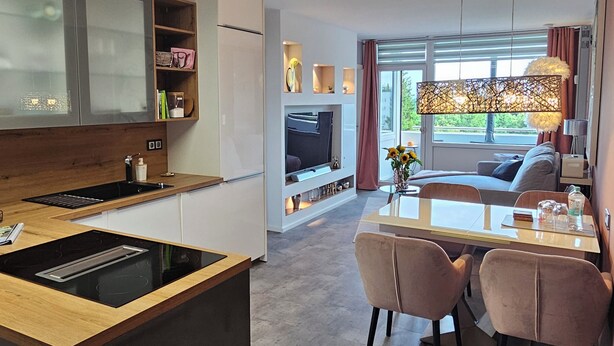 Una cocina moderna con una isla central, un comedor con mesa y sillas, y un espacio de estar con sofá y televisor.