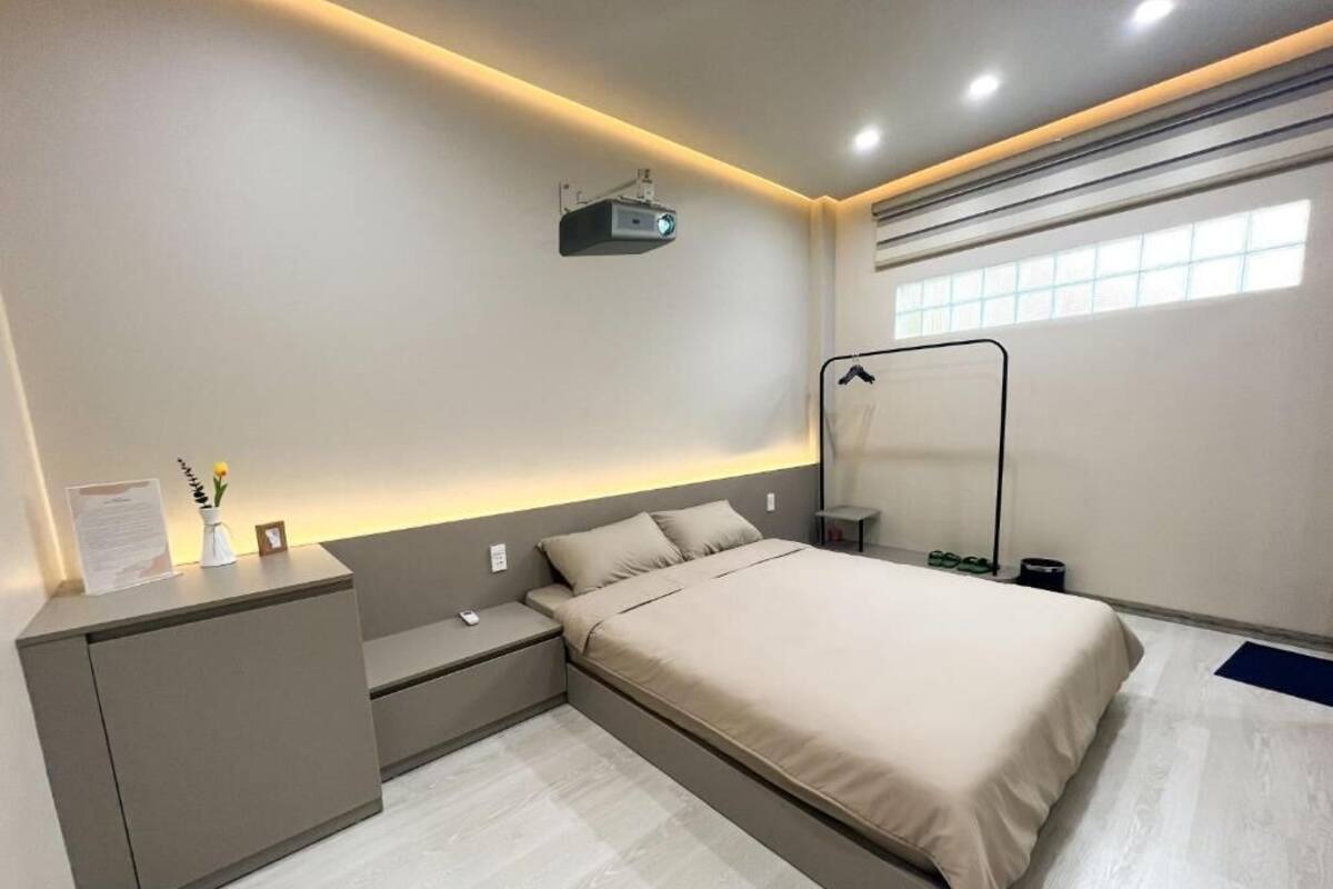 Un dormitorio moderno con cama, mesitas de noche, un mueble pequeño, un proyector y una ventana con persianas.