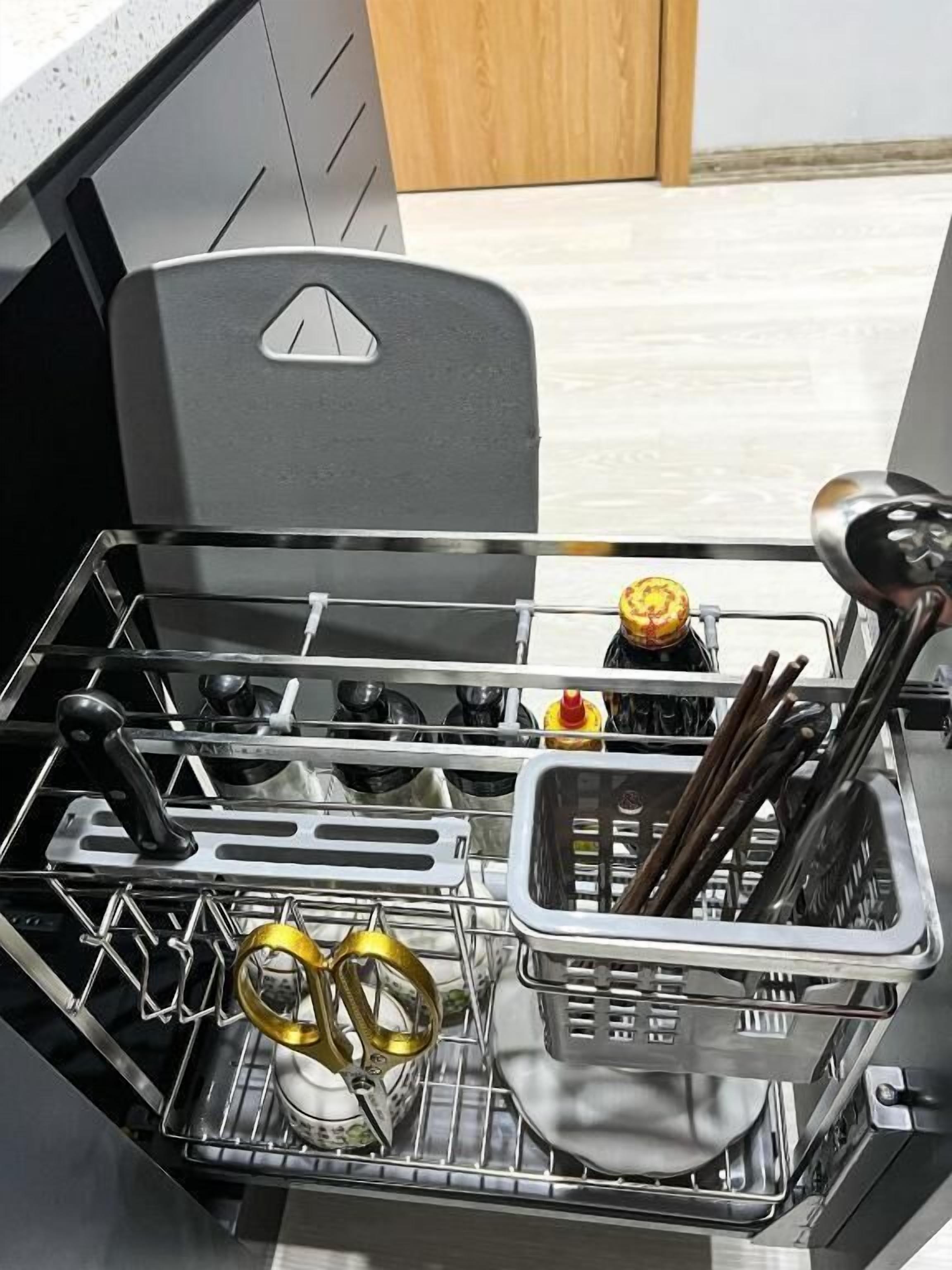 A kitchen with a dishwasher, utensils, and a bottle of ketchup.