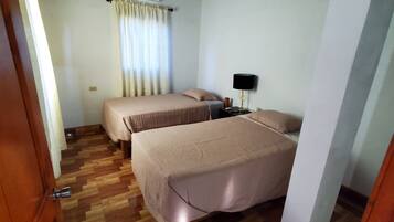 A room with two beds, a ceiling fan, an air conditioning unit, and a wooden floor.