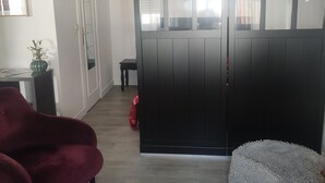 Un salón con un sillón rojo, una cama para mascotas color gris, una mesa de centro de madera con una planta y un control remoto, y una puerta corredera negra.