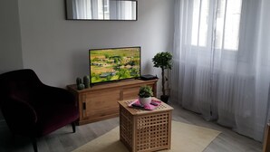 Una sala de estar con una televisión, un mueble de madera, una mesita con una planta y un sillón rojo.