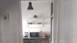 Una cocina compacta con microondas, un taburete pequeño y una lámpara colgante.