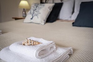 A neatly folded white towel with a decorative item on a bed with a textured white cover. - UR-SUN&SEA DOWNTOWN APARTMENT WITH VERANDA (Villasimius)