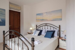A bedroom with a bed, a nightstand, a lamp, a painting, and a wooden door. - UR-SUN&SEA DOWNTOWN APARTMENT WITH VERANDA (Villasimius)