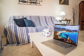 A striped sofa, a laptop on a table, and a vase with a coastal scene on the screen. - UR-SUN&SEA DOWNTOWN APARTMENT WITH VERANDA (Villasimius)