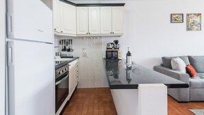 Una cocina compacta con armarios blancos, encimera negra y un sofá gris en la sala de estar.