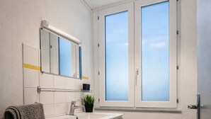 A modern bathroom with a wooden vanity, a mirror, a window, and a hanging light fixture.