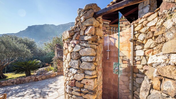 Un edificio de piedra con puerta de cristal, un camino de piedra y montañas al fondo.