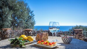 Una mesa con comida, una copa de vino blanco y vista al mar.