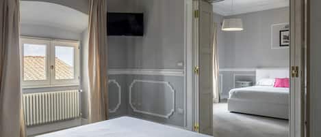 Un dormitorio con cama, televisión, radiador y ventana con cortinas.