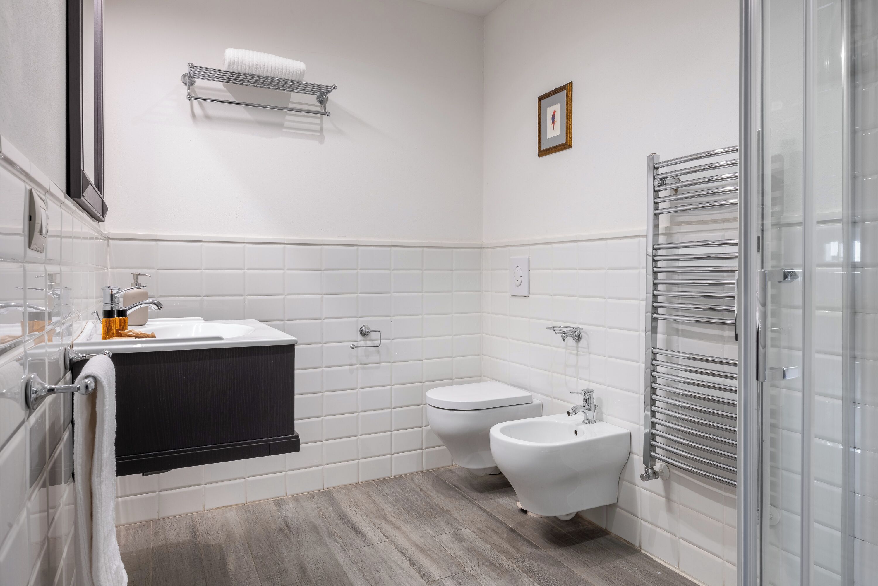 Ein modernes Badezimmer mit weißem Waschbecken, Toilette, Bidet und einer Duschkabine aus Glas.