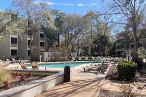 A pool area with lounge chairs, a swimming pool, and surrounding trees. - Charming condo with screened balcony, central AC, close to beach & golf (Myrtle Beach)