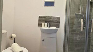 Et badeværelse med toilet, håndvask, brusebad og et lille spejl.
