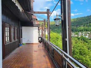 Ein Balkon mit Terrakottafliesen, Holzgeländern und Blick auf eine grüne Landschaft.