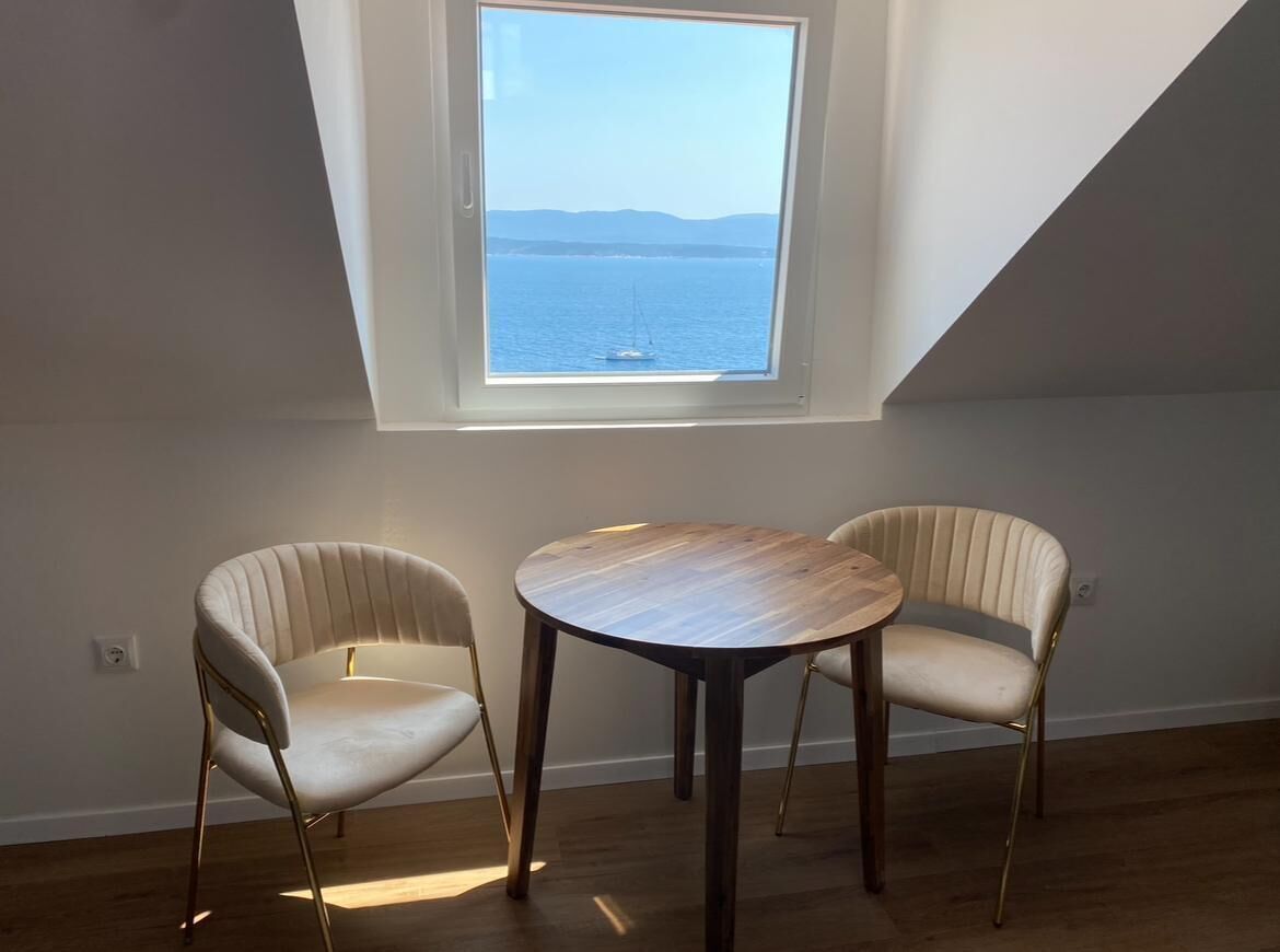 Una habitación con tragaluces, dos sillas, una mesa redonda y vista al mar.