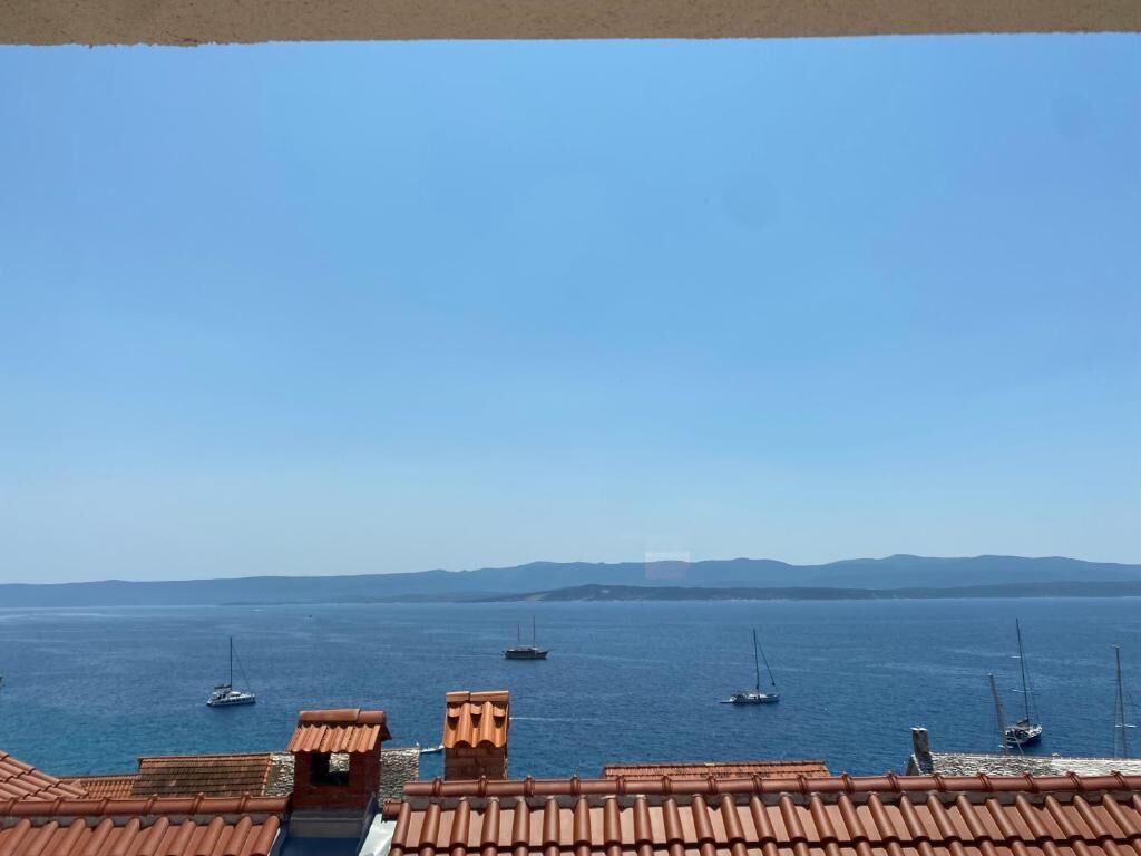 Blick auf die Küste mit blauem Himmel, einem Meer mit Booten und terrakottafarbenen Dächern.