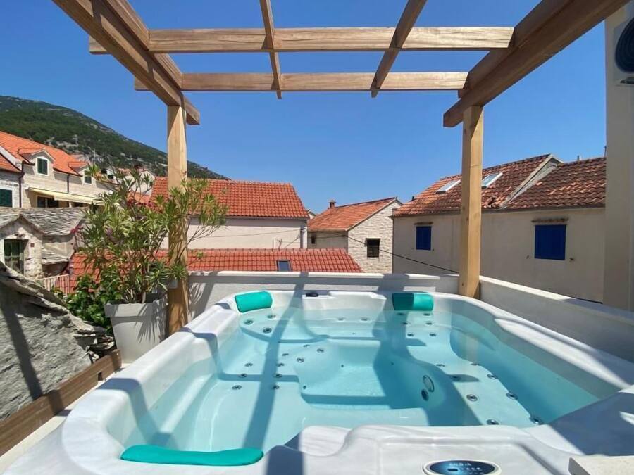 A hot tub under a wooden pergola with a clear view of red-tiled buildings in the background.