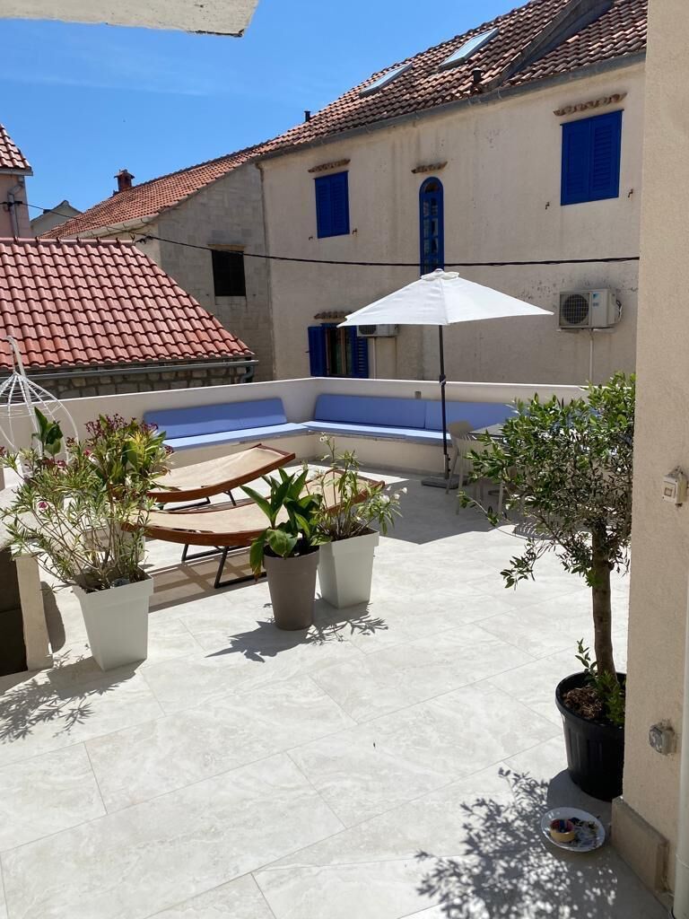 A rooftop terrace with potted plants, a white umbrella, and a pool.