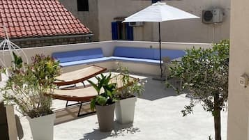 A rooftop terrace with potted plants, a white umbrella, and a pool.