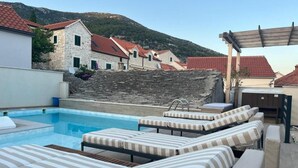 Ein Poolbereich mit Liegestühlen, einer Pergola und Gebäuden aus Stein im Hintergrund.