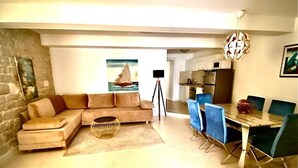 Ein Wohnzimmer mit Sofa, Esstisch mit Stühlen, Küchenzeile und einem Bild an der Wand.