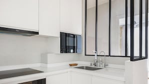 Eine moderne Küche mit weißen Schränken, einem Kochfeld von Bosch, einer Spüle aus Edelstahl und einem Fenster mit Jalousien.