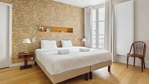 Ein Hotelzimmer mit einem großen Bett, einem Nachttisch aus Holz, einem Sessel, einem Deckenventilator und einem Fenster mit Vorhängen.