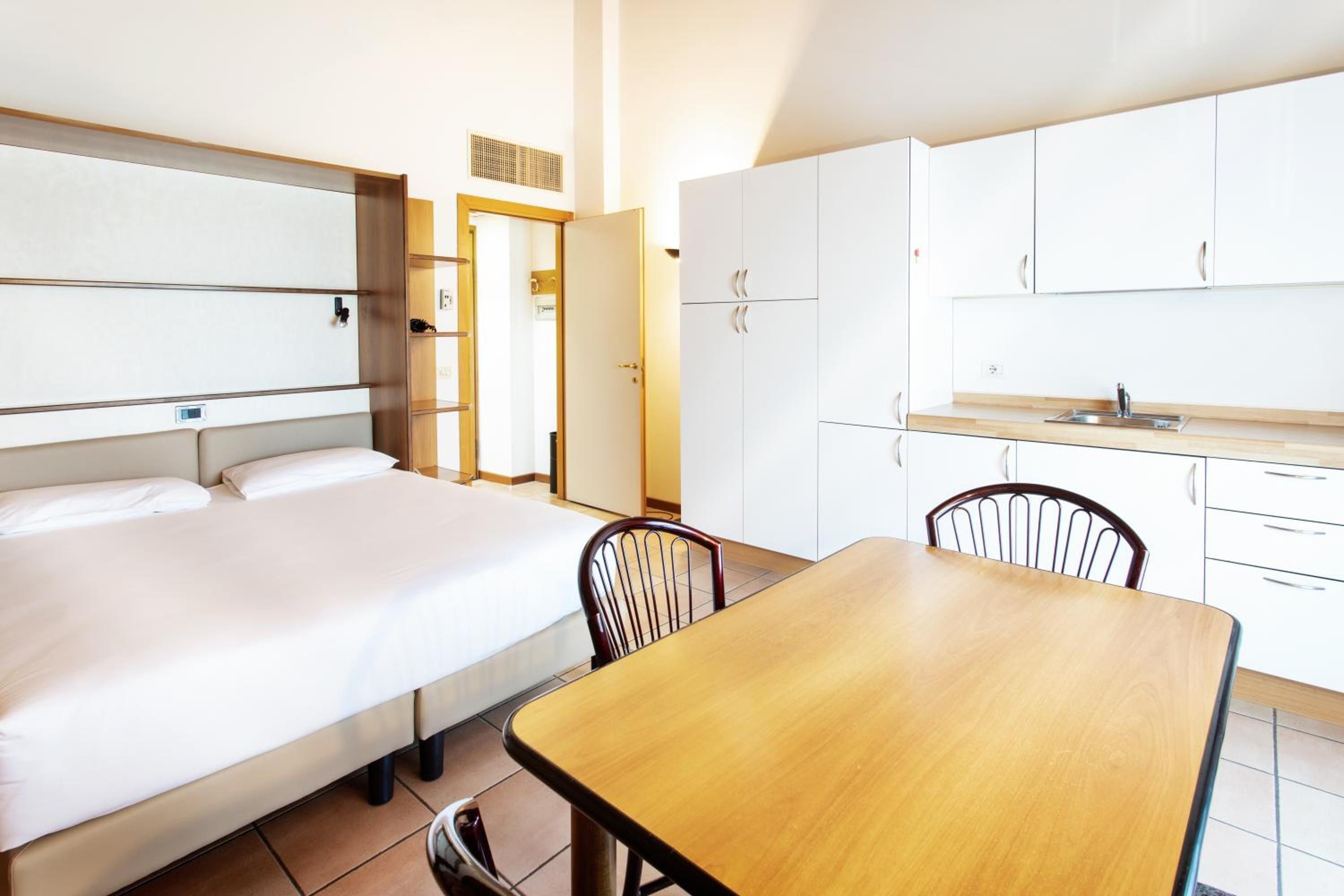 A hotel room with a bed, a wooden table, and a kitchenette.