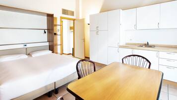 Una camera d'albergo con un letto, un tavolo di legno e angolo cottura.
