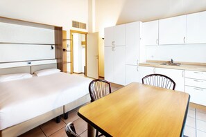 A hotel room with a bed, a wooden table, and a kitchenette. - Residenza Le Cupole (Parma)