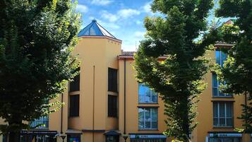 Un edificio a più piani con facciata gialla, diverse finestre e un tetto blu. In primo piano si vedono auto parcheggiate e un cartello con la scritta 'La Cassa'.