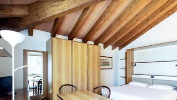 Ein Zimmer mit Holzbalkendecke, einem Bett, einem Esstisch mit Stühlen und einem Fernseher.