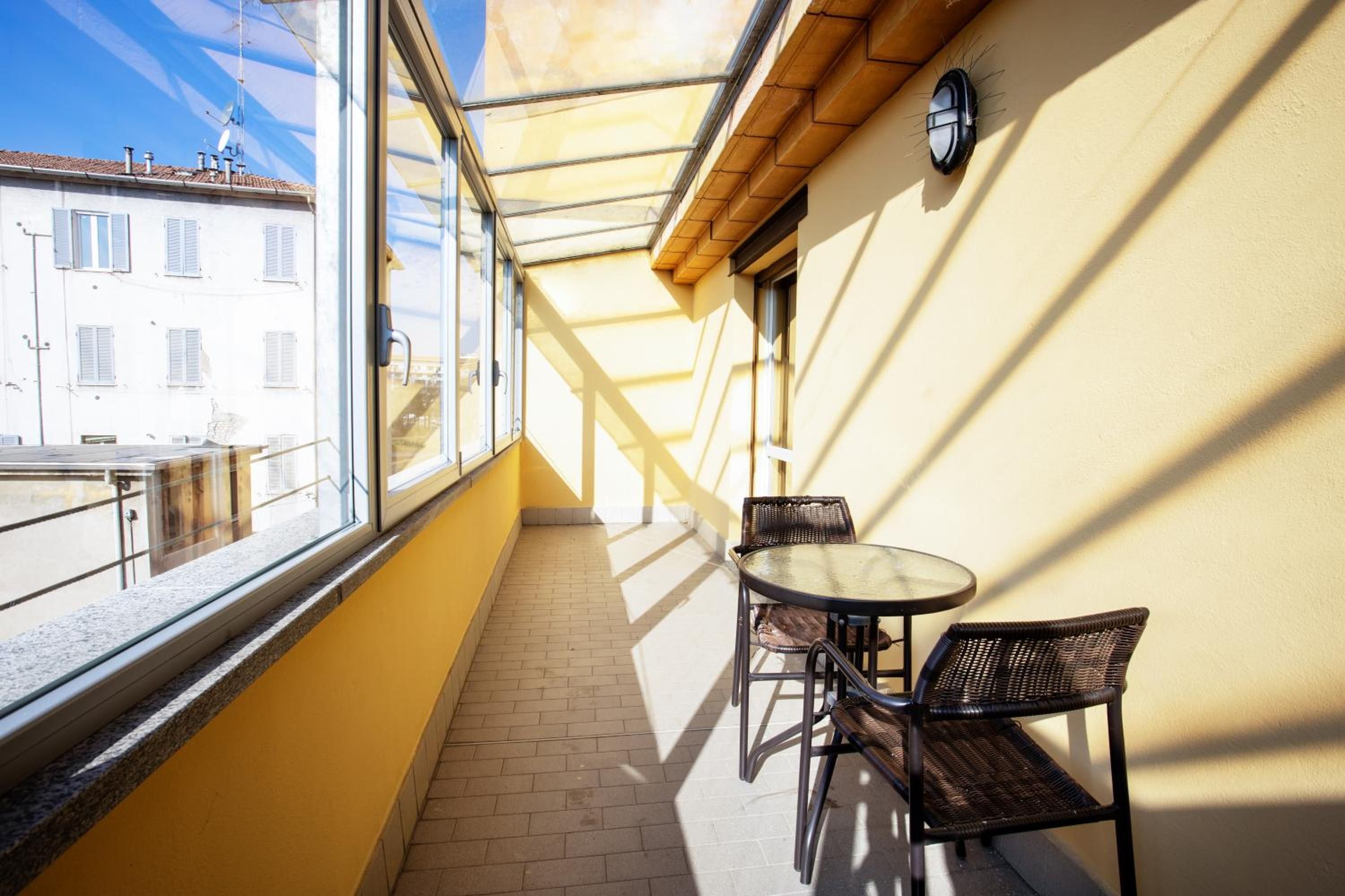 A balcony with a table and chairs, a view of buildings, and a clock on the wall.