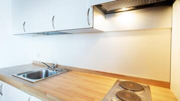 Una cucina con lavello in acciaio inox, piano di lavoro in legno, mobili bianchi e piano cottura elettrico integrato.