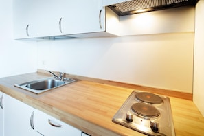 A kitchen with a stainless steel sink, wooden countertop, white cabinets, and a built-in electric stove. - Residenza Le Cupole (Parma)